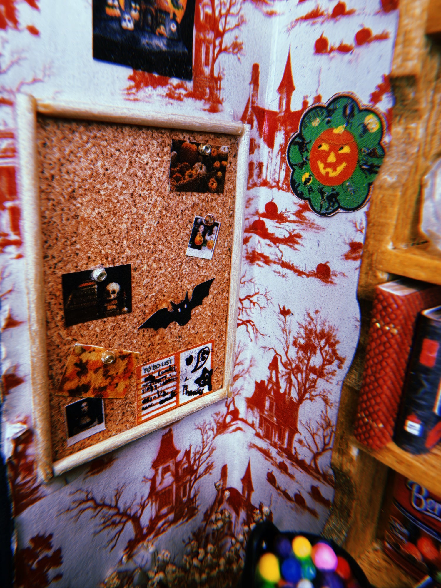 Haunted house patterned wallpaper with decorations and a cork bulletin board full of Halloween-themed pins and photos.