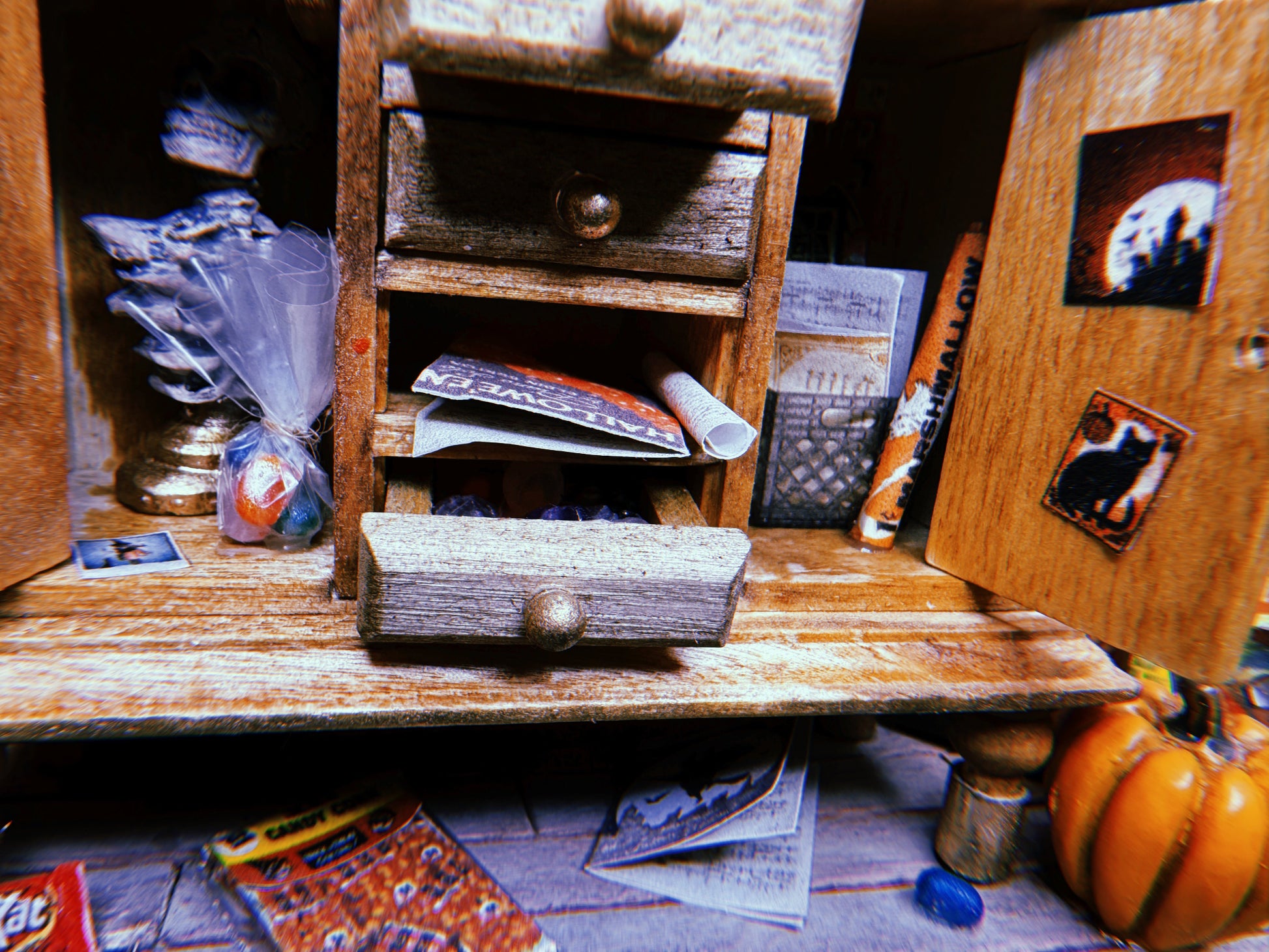 Close up of the bottom cabinets which open to reveal bags of candy, Halloween posters, postcards and photographs. Bags of candy corn, jelly beans and candy bars are strewn across the floor.