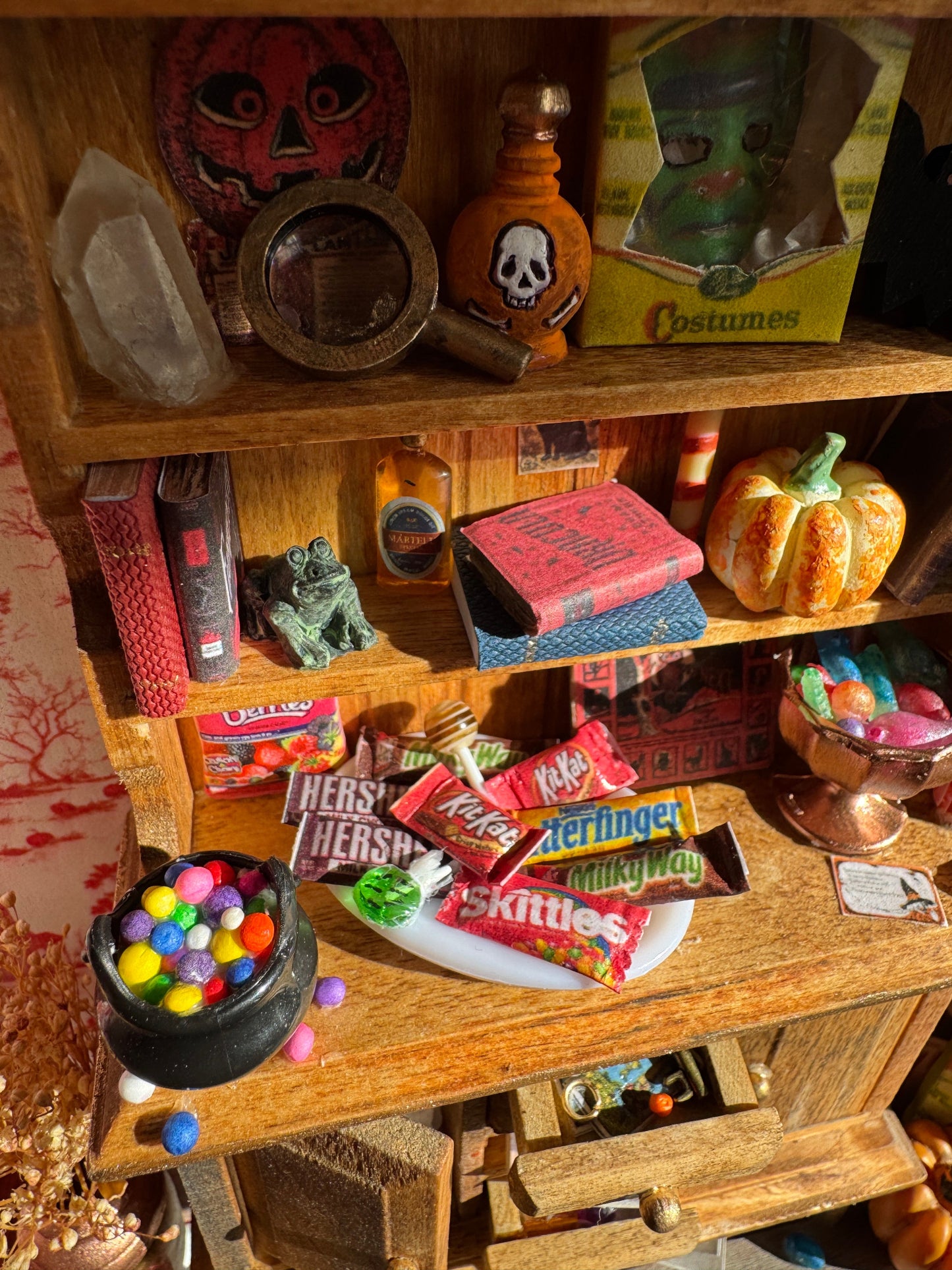Close ups of the shelves from another angle showing crystals, a magnifying glass, horror books, potion bottles, pumpkins, board games, a pumpkin, a halloween mask, trays of candies and other trinkets.