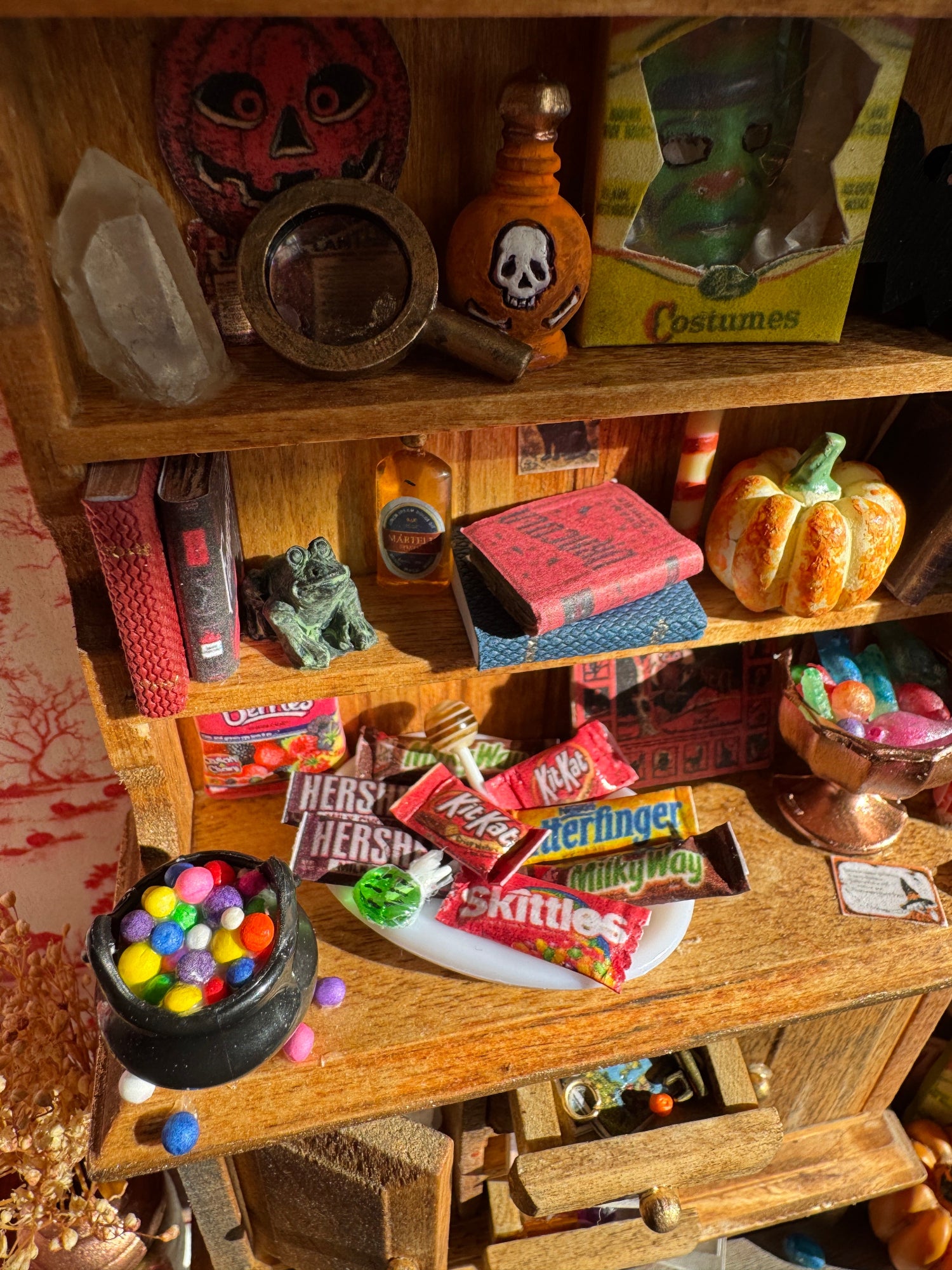 Close ups of the shelves from another angle showing crystals, a magnifying glass, horror books, potion bottles, pumpkins, board games, a pumpkin, a halloween mask, trays of candies and other trinkets.
